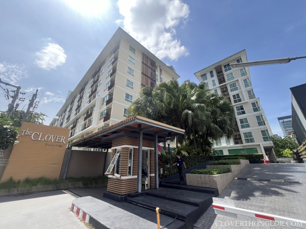Main entrance and security gatehouse of The Clover Thonglor Residence, a modern low-rise condominium in Bangkok, with tropical landscaping and blue sky.