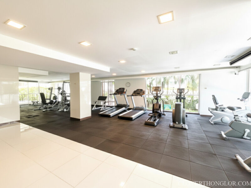 equipment in the gym 1 Wide view of The Clover Thonglor's brightly lit gym, showcasing a full range of modern cardio machines and weight stations on black rubber flooring.