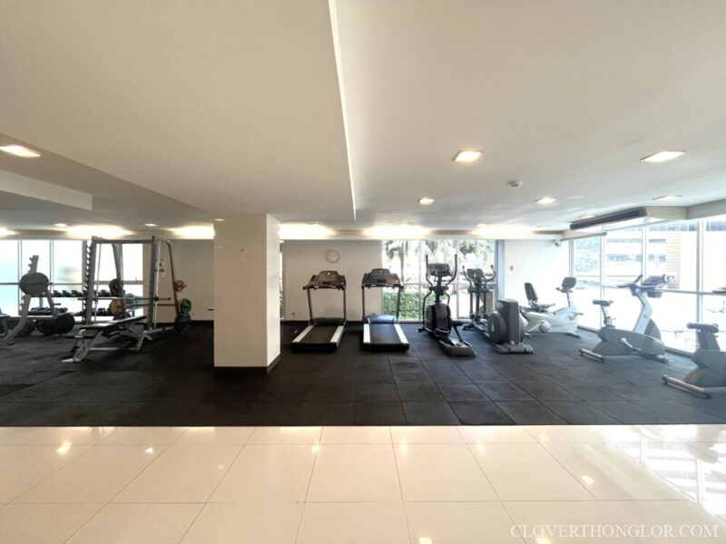 Well-equipped fitness center at The Clover Thonglor. Features cardio machines (treadmills, ellipticals) and weight training stations on a rubber floor.