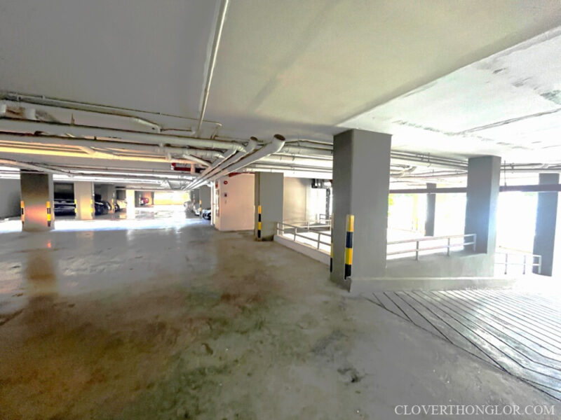 Interior of the multi-level parking garage at The Clover Thonglor, showing the ample, brightly lit space and the ramp leading to the next floor.
