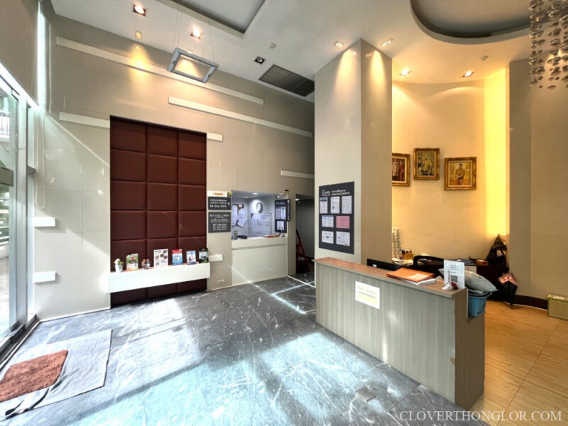 Lobby area at The Clover Thonglor: Juristic Person's reception desk with a modern wood finish, and an adjacent waiting or information area.